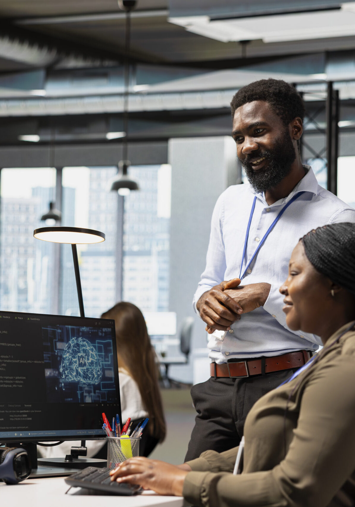 Smiling AI tech startup workplace team leader reviewing performance of worker optimizing code on PC. Satisfied supervisor providing positive feedback to engineer working with artificial intelligence