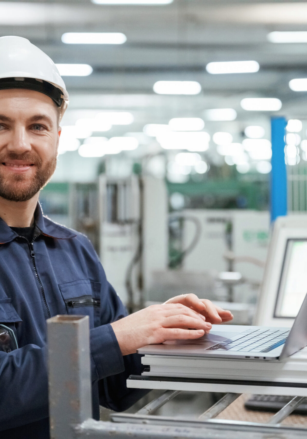 Using the laptop. Factory worker is indoors with hard hat.