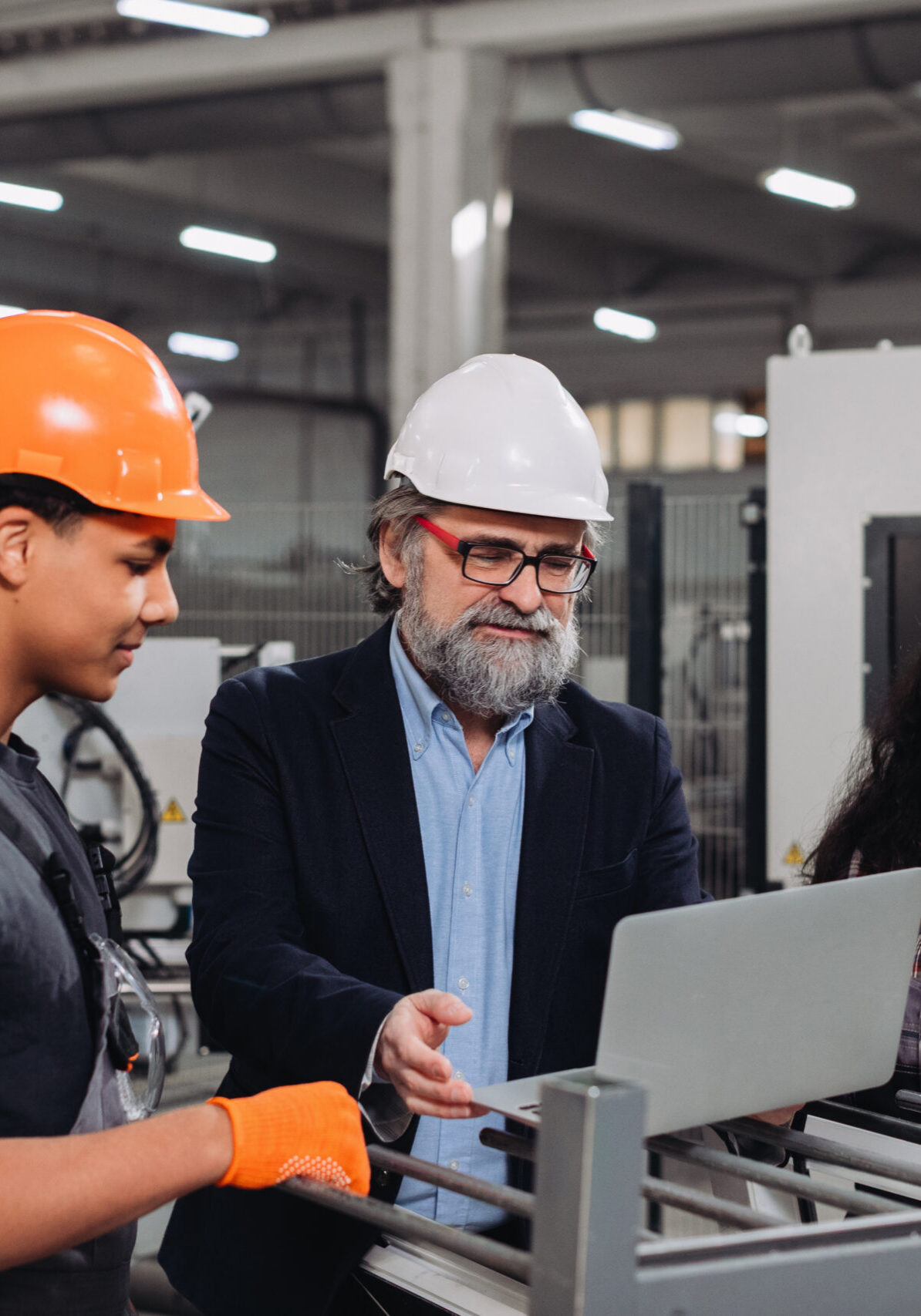 Industrial manager guiding diverse young employees, discussing manufacturing processes on a laptop in a modern production facility